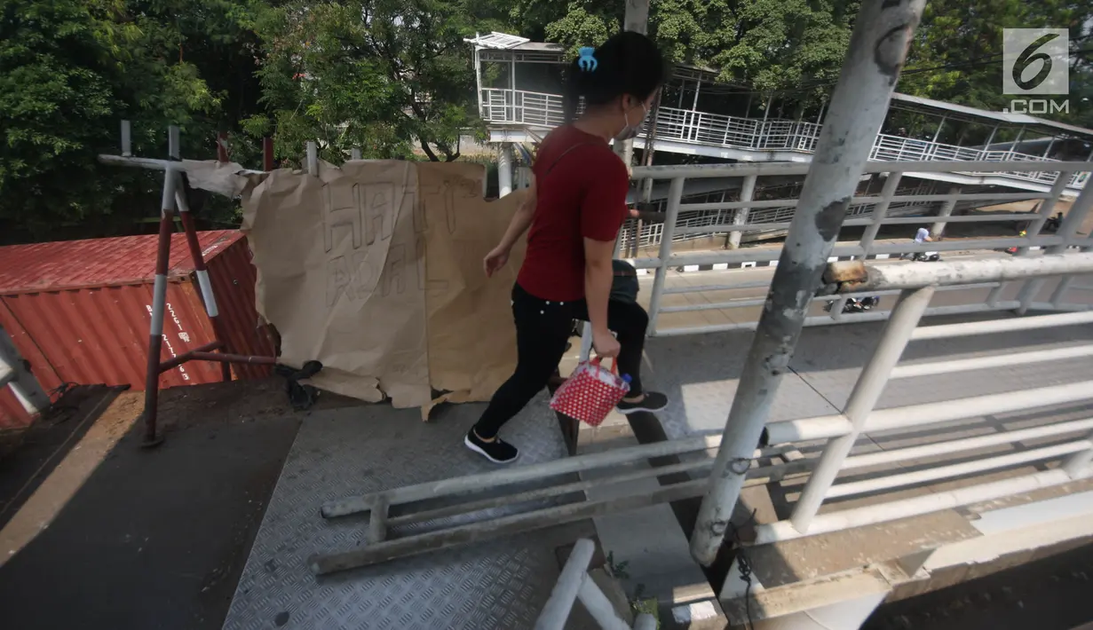 Pejalan kaki melewati lubang di atas JPO di Halte Bus Transjakarta di Jembatan Gantung, Cengkareng, Jakarta, Jumat (27/7). JPO yang rusak akibat tertabrak truk sejak setahun lalu hingga kini belum diperbaiki.  (Liputan6.com/Arya Manggala)