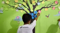 Seorang bocah tengah menempelkan kertas bertuliskan asa di pohon harapan. (Liputan6.com/Muhammad Ali)