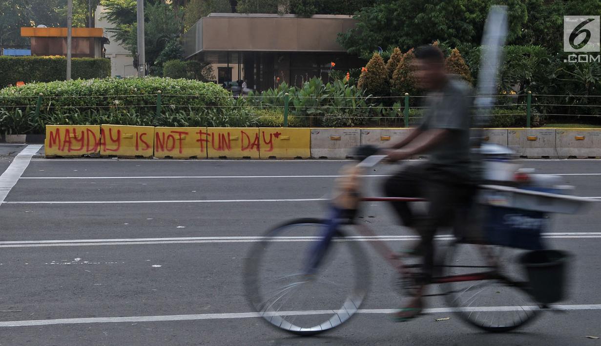 Pedagang siomay melintasi coretan "May Day Is Not Fun Day" di pembatas jalur bus Transjakarta kawasan Sarinah, Jakarta, Selasa (1/5). Aksi May Day di Jakarta meninggalkan jejak vandalisme yang dibuat kaum pekerja itu. (Merdeka.com/ Iqbal S. Nugroho)