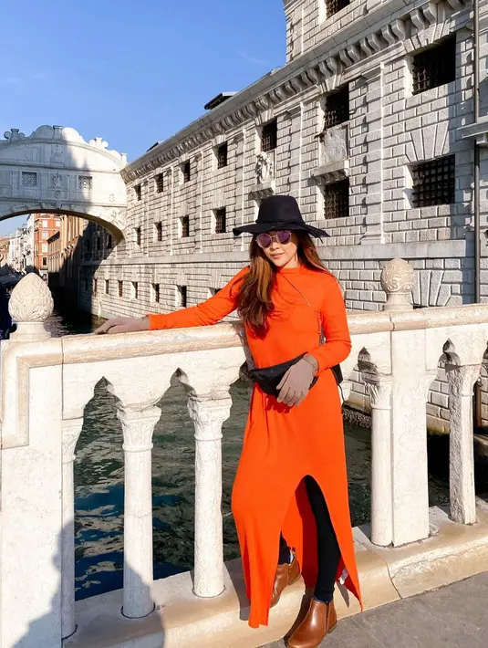 Gaya bohemian dengan tunic oranye, boater hat, dan sepatu boots kala berlibur di Italia. [Foto: IG/jenny.mci8].