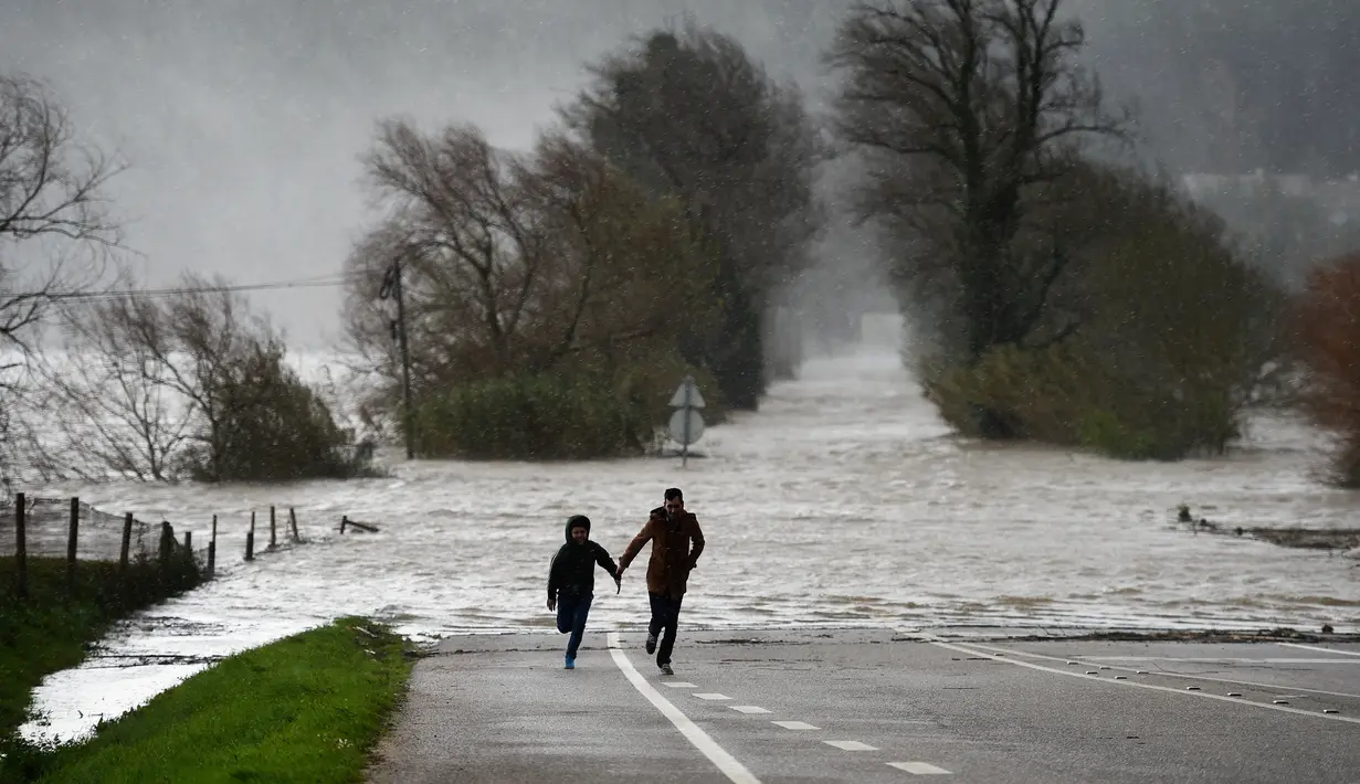 Seorang ayah dan anaknya berlari untuk berlindung dari luapan air yang terjadi di Arzila, Portugal (14/2/2016). Angin kencang dan pohon tumbang menyebabkan gangguan di jalan utama kota tersebut. (AFP Photo /Francisco Leong)