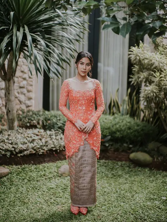 Adinda Thomas terlihat cerah di hari Lamaran dengan kebaya simple orange dari Ayung Berinda. Kebaya H-Line itu punya cross cut di bagian bawah dipadukan dengan kain Tenun keemasan [@ayungberinda]