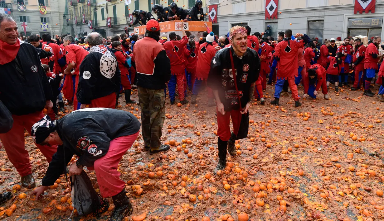 Peserta berjalan di atas tumpukan jeruk yang hancur pada festival "Battaglia delle Arance" (Perang Jeruk) di sebuah kota kecil di Provinsi Turin, Italia, Minggu (11/2). Tradisi melempar jeruk dilakukan selama tiga hari pada Februari. (MIGUEL MEDINA/AFP)