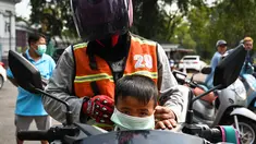 Seorang anak laki-laki mengenakan masker saat dijemput dari sekolah di Bangkok (30/1). Polusi buruk memaksa pemerintah Bangkok mengeluarkan perintah untuk meliburkan 450 sekolah pada 30 Januari. (AFP Photo/Lillian Suwanrumpha)