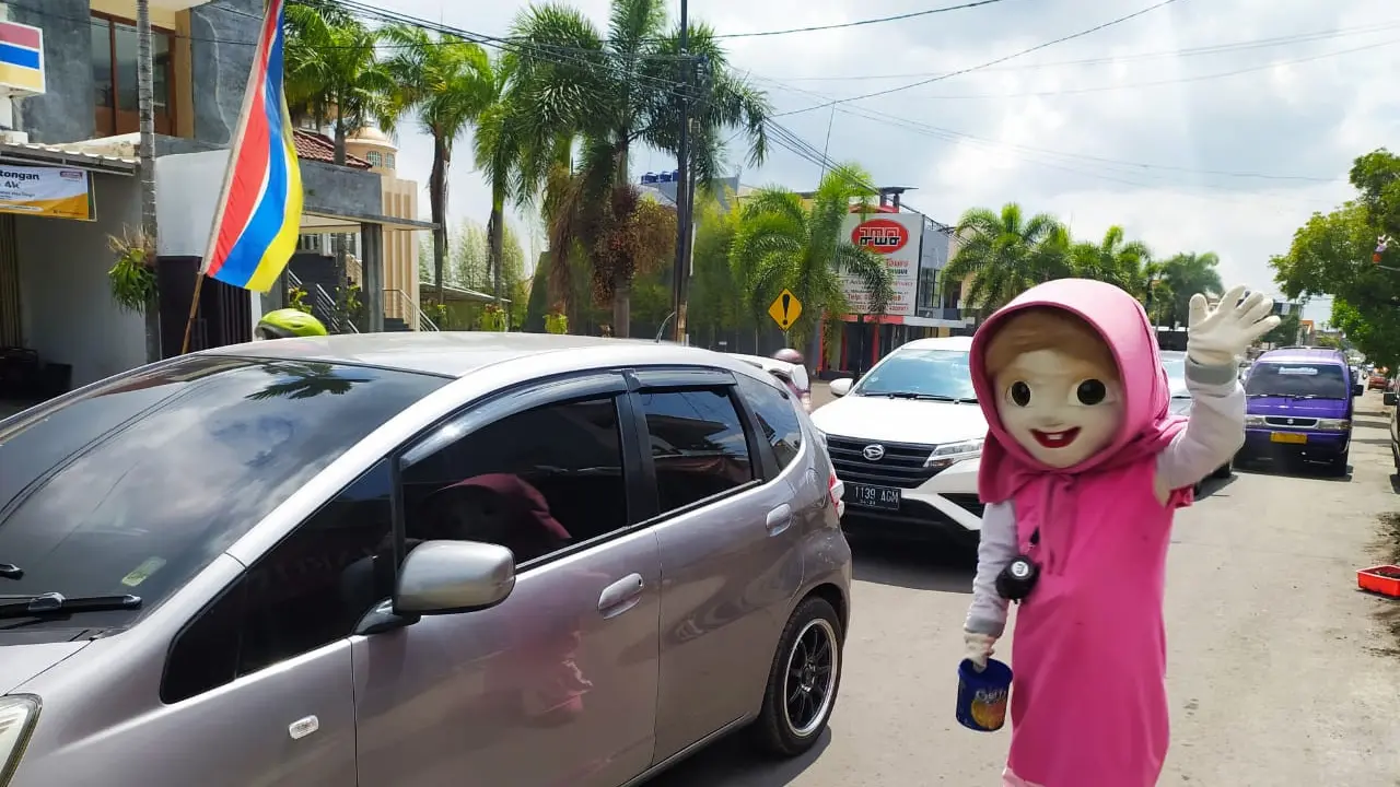 Dengan warna cerah, seorang pengamen boneka karaktek 'Marsha' terlihat menggemaskan memberikan hiburan tersendiri bagi pejalan kaki dan pengguna yang tengah melintas di pinggir jalan.
