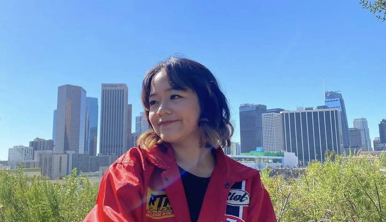 Berada di Amerika, Cinta tampil mengenakan jaket merah dipadukan t shirt hitamnya. Rambut pendeknya bergaya wave diwarnai coklat di bagian bawah. [@cintakuya]