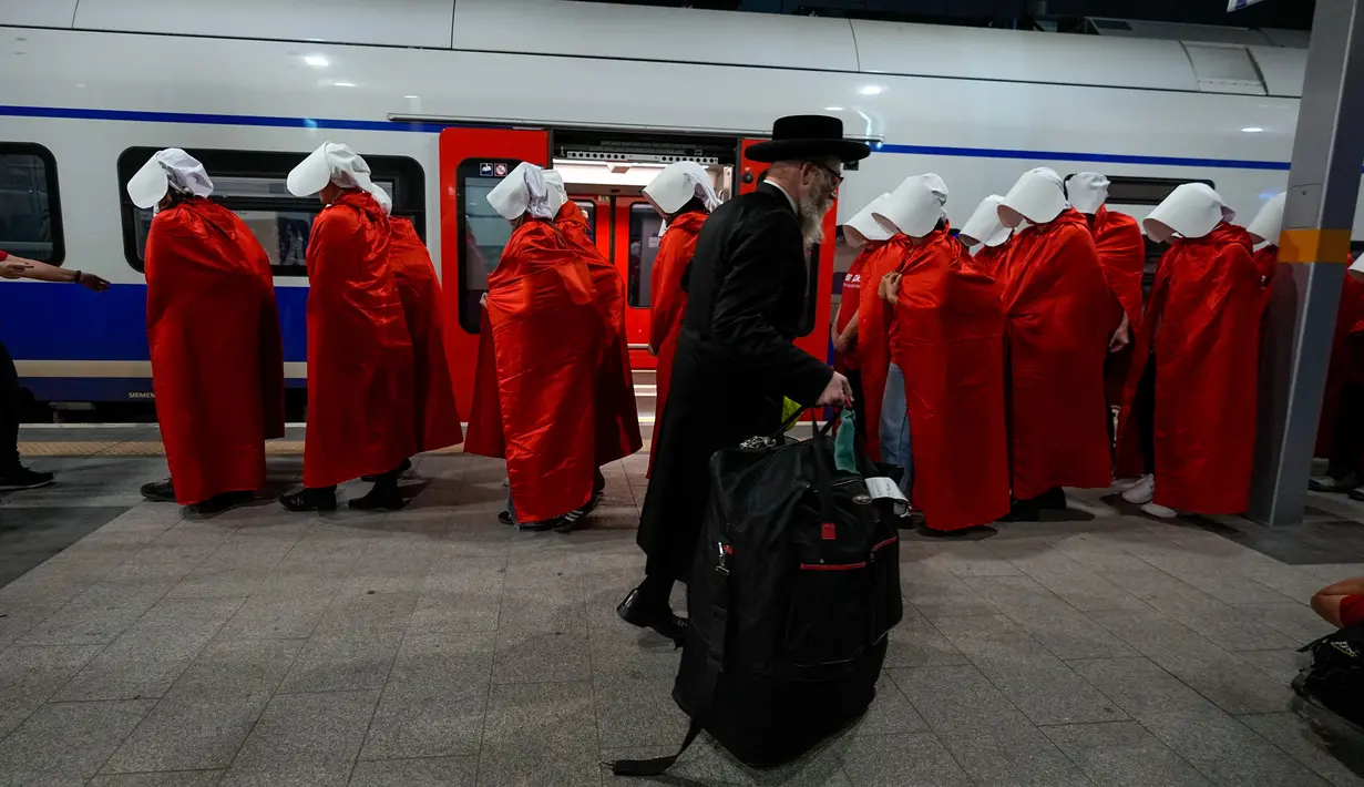 Pengunjuk rasa yang mendukung hak-hak perempuan berpakaian seperti karakter dari serial TV "The Handmaid's Tale" saat melakukan perjalanan untuk memprotes rencana pemerintah baru Perdana Menteri Benjamin Netanyahu untuk merombak sistem peradilan di sebuah stasiun kereta api di Yerusalem, Israel, 1 Maret 2023. Mengacu pada fenomena yang berkembang, harian Inggris The Guardian menggambarkan penampilan para pelayan sebagai salah satu simbol paling kuat dari protes feminis kontemporer. (AP Photo/Ohad Zwigenberg)