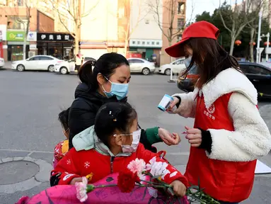 Relawan masyarakat Wang Shujia (kanan) memeriksa suhu tubuh warga di Hefei, Provinsi Anhui, China timur (5/3/2020). Wang Shujia, seorang mahasiswi, ambil bagian dalam tim relawan masyarakat di Hefei untuk membantu mencegah dan mengendalikan epidemi virus corona. (Xinhua/Liu Junxi)