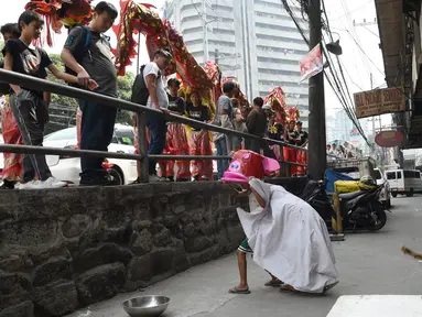 Anggota kelompok barongsai melihat aksi anak-anak melakukan tarian singa di distrik Chinatown, Manila (4/2). Anak-anak jalanan ini tampil lucu dengan alat seadanya seperti ember dan kerdus untuk menyambut Tahun Baru Imlek. (AFP Photo/Ted Aljibe)