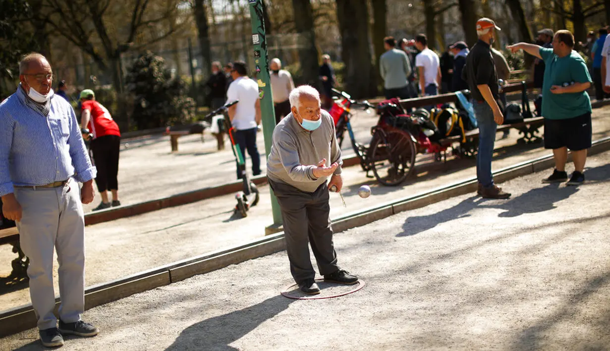 Seorang pria mengenakan masker untuk mencegah penyebaran COVID-19 saat memainkan boule di Taman Cinquantenaire, Brussel, Belgia, Senin (29/3/2021). Belgia kembali memberlakukan lockdown ketat sebagai tanggapan atas lonjakan infeksi COVID-19 yang mengkhawatirkan. (AP Photo/Francisco Seco)