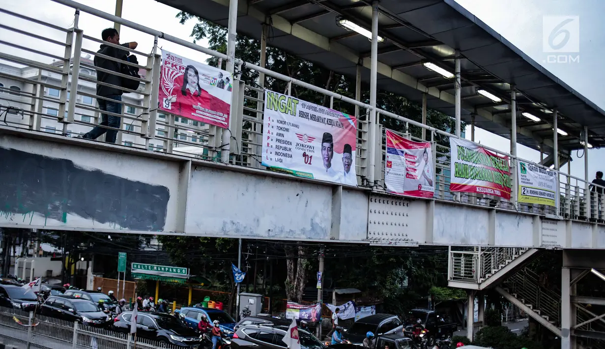 Warga melintasi jembatan penyeberangan orang (JPO) yang terdapat alat peraga kampanye (APK) di Mampang, Jakarta, Rabu (27/2). APK masih menghiasi JPO meski KPU telah melarang pemasangan di sarana dan prasarana publik. (Liputan6.com/Faizal Fanani)