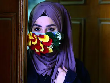 Seorang perempuan mengenakan topeng yang dihiasi kelopak bunga di tengah virus corona (Covid-19) di pusat kota suci Najaf, Irak pada 21 Maret 2020. Masker dijadikan masyarakat pilihan untuk mencegah penyebaran pandemi virus corona yang terus meningkat di seluruh dunia. (Haidar HAMDANI/AFP)