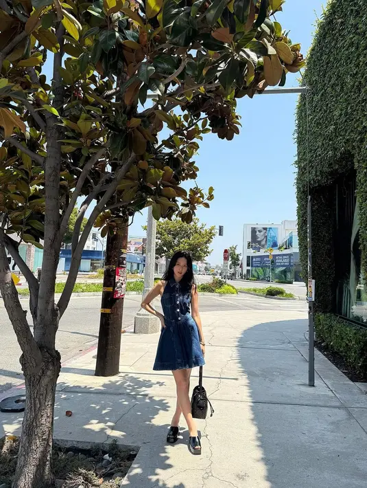 Bucket bag hitam itu juga lengkapi denim sleeveless dress Jisoo BLACKPINK dengan open toe wedges [Dior]