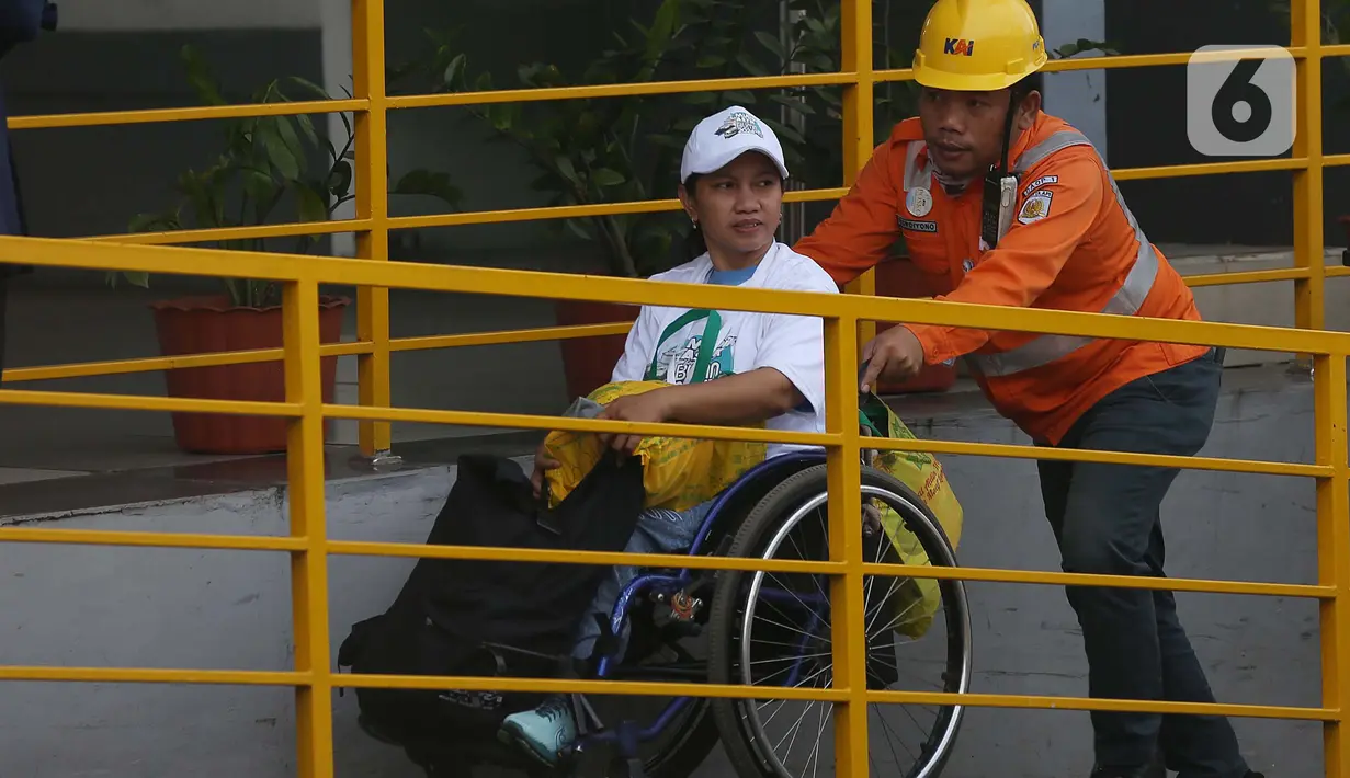 Pekerja PT Kereta Api Indonesia (Persero) membantu salah satu penyandang disabilitas yang mengikuti program Mudik Gratis di Stasiun Pasar Senen, Jakarta, Minggu (7/4/2024). (Liputan6.com/Helmi Fithriansyah)