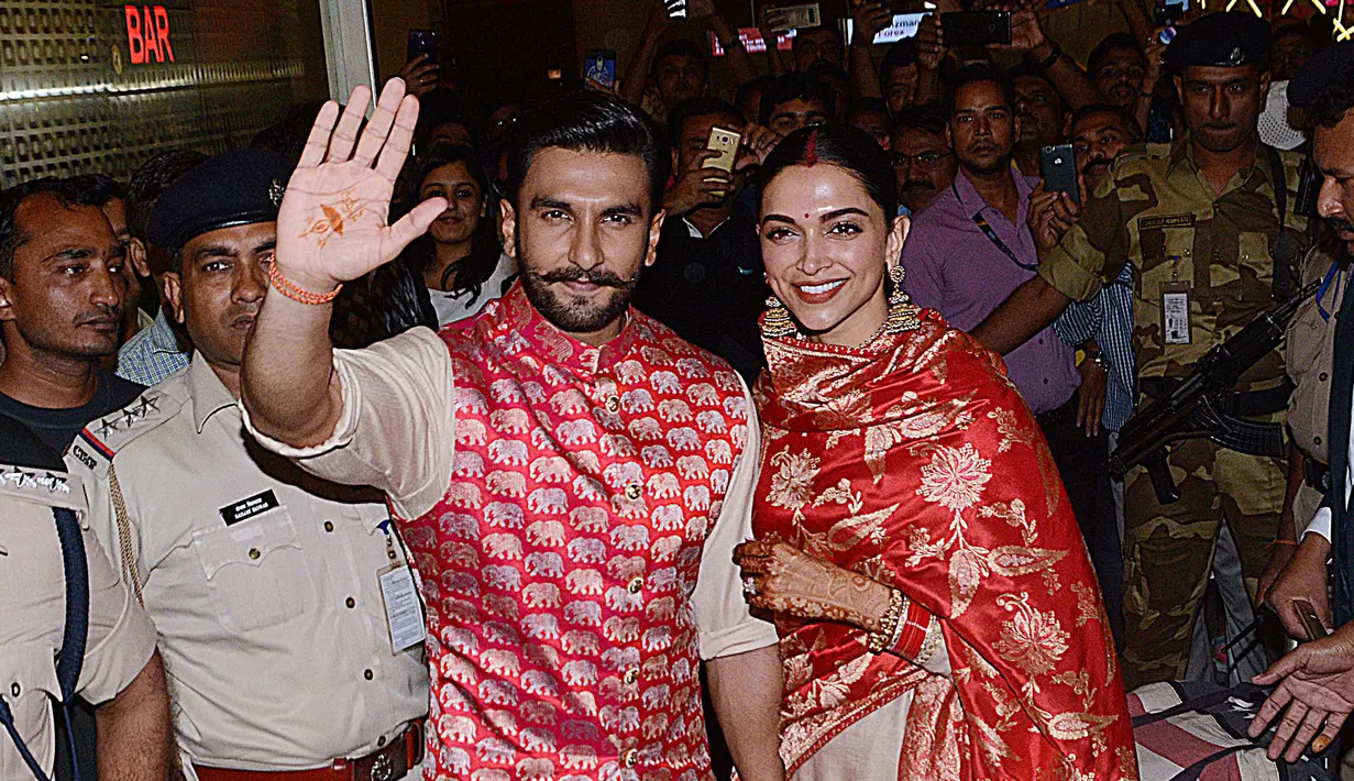 Pasangan pengantin baru, Ranveer Singh dan Deepika Padukone menyapa penggemar yang menyambut mereka di bandara internasional Mumbai, Minggu (18/11). Pasangan bintang Bollywood India itu baru saja kembali dari acara pernikahan mereka di Italia. (AFP)