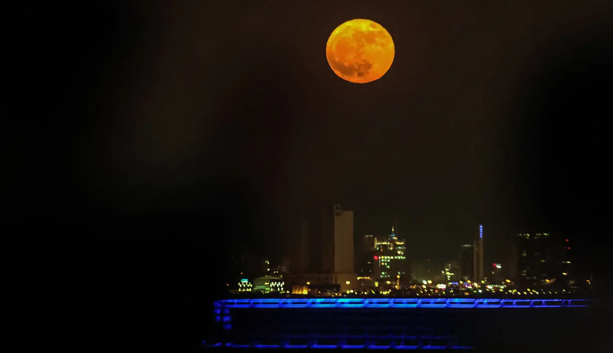 Orang-orang menyaksikan bulan penuh yang disebut sebagai Buck Moon  terbit di atas cakrawala Kota Kuwait pada Senin, 3 Juli 2023. (YASSER AL-ZAYYAT / AFP)
