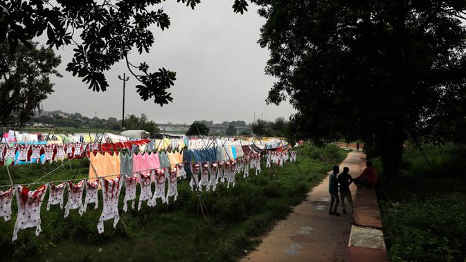Dhobis, atau tukang cuci, menunggu pakaian yang digantung kering di antrean setelah dicuci di tepian Sungai Gomti di Lucknow, India, 12 September 2020. Dhobi adalah pekerja binatu tradisional yang mencuci pakaian dengan tangan dan menjemurnya di bawah sinar matahari. (AP Photo/Rajesh Kumar Singh)