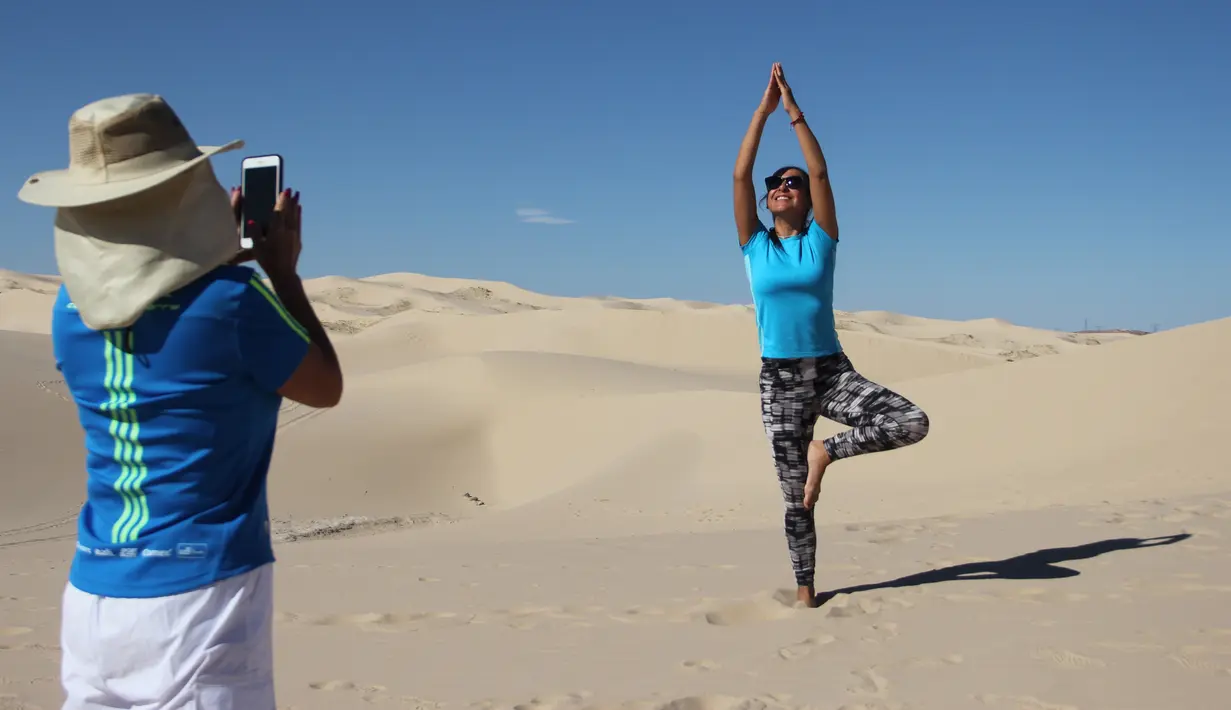 Seorang wanita berpose selama kelas yoga yang diselenggarakan oleh komunitas YSYoga System di gurun Samalayuca, negara bagian Chihuahua, Meksiko pada 25 Mei 2019. Kelas yoga di padang pasir ini diselenggarakan setiap tahun, dan pesertanya semakin lama semakin bertambah banyak. (Herika MARTINEZ/AFP)