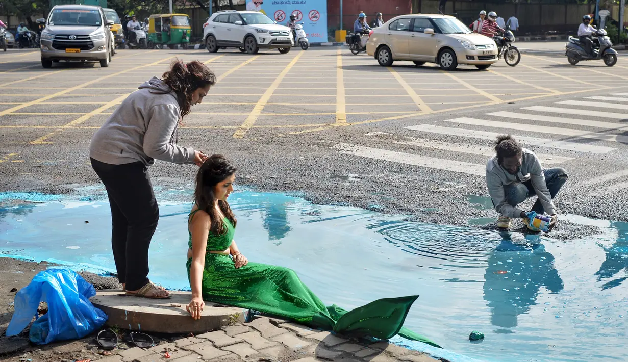 Seorang model berpakaian seperti putri duyung ambil bagian dalam seni instalasi seniman Baadal Nanjundawsamy di Bangalore, India, 13 Oktober 2107. Aksi unik seniman asal Bengaluru itu dilakukan untuk mengkritik pemerintah. (MANJUNATH KIRAN / AFP)