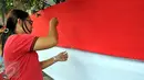 Seorang warga terlihat serius menjahit bendera merah putih saat mengikuti lomba di Kelurahan Pekojan, Jakarta, Minggu (16/8/2015). Lomba memperebutkan trofi lurah dan sejumlah uang. (Liputan6.com/Panji Diksana)