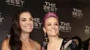Penyerang Amerika Serikat, Megan Rapinoe bersama Alex Morgan berpose saat tiba menghadiri penghargaan sepak bola FIFA Terbaik, di teater La Scala Milan, Italia utara (23/9/2019). Rapinoe tampil seksi mengenakan gaun hitam dengan belahan dada rendah. (AP Photo/Luca Bruno)