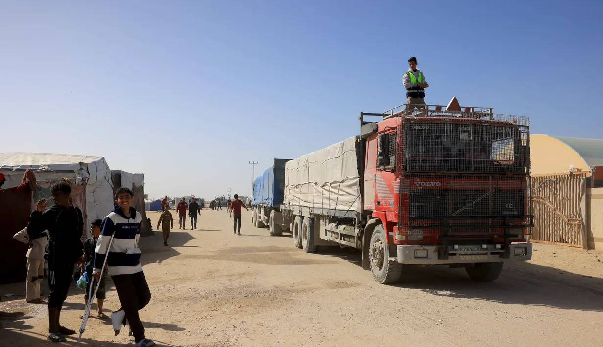 Sebelum Israel melancarkan perang di Gaza, Rafah merupakan jalur penyeberangan utama orang-orang yang keluar masuk wilayah Palestina. Tampak dalam foto, warga Palestina menyaksikan truk-truk yang membawa bantuan kemanusiaan tiba di Khan Yunis di Jalur Gaza selatan, setelah melewati penyeberangan perbatasan Rafah dari Mesir, pada 1 Februari 2026. (Bashar Taleb/AFP)