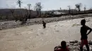 Dua bocah mengamati warga yang berusaha menyeberangi sungai beraliran deras di Les Anglais, 10 Oktober 2016. Selain merusak ribuan rumah, badai Matthew di Haiti juga memutus jembatan yang merupakan akses utama warga. (REUTERS/Andres Martinez Casares)