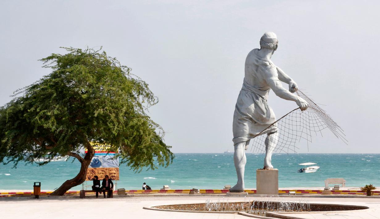 Sepasang suami istri duduk di dekat patung raksasa di tepi laut, Pulau Kish di Iran, 1 November 2016. Di pulau ini hukum Islam tidak seketat seperti tempat lainnya di Iran, dengan harapan bisa menarik mereka berkunjung. (Atta Kenare/AFP)