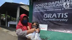 Seorang ibu menggendong anaknya sambil membawa nasi bungkus yang disediakan gratis di Kompleks Sinar Pamulang Permai, Pamulang Barat, Tangerang Selatan, Senin (13/4/2020).  (merdeka.com/Arie Basuki)