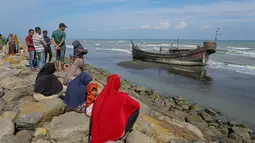 Penduduk desa melihat perahu kayu yang digunakan oleh orang-orang Rohingya di Pidie, provinsi Aceh pada 27 Desember 2022. Pengungsi Rohingya menerima perawatan medis darurat setelah sebuah kapal yang membawa hampir 200 orang mendarat di Indonesia pada 26 Desember, kata pihak berwenang, dalam pendaratan keempat di negara dalam beberapa bulan terakhir. (AFP/Amanda Jufrian)