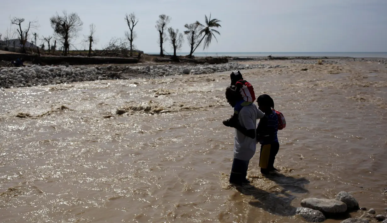 Seorang warga menggendong anaknya sambil berusaha menyeberangi sungai di Les Anglais, 10 Oktober 2016. Selain merusak ribuan rumah, badai Matthew di Haiti juga memutus jembatan yang merupakan akses utama warga. (REUTERS/Andres Martinez Casares)