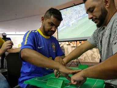 Suporter Brasil yang buta dan tuli, Carlos Junior merasakan berlangsungnya pertandingan 16 besar Piala Dunia 2018 antara Brasil melawan Meksiko dibantu penerjemah dengan miniatur lapangan sepak bola di Sao Paulo, Brasil, (2/7). (AP Photo / Nelson Antoine)