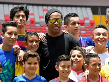 Mantan bintang sepak bola Brasil Ronaldinho berpose dengan anak-anak Kosta Rika sebelum pertandingan persahabatan melawan mantan pemain Kosta Rika di Stadion Nasional di San Jose, (4/8). (AFP Photo/Ezequiel Becerra)