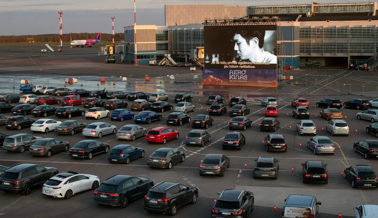 Orang-orang duduk di mobil mereka saat menonton film di bioskop drive-in di area apron bandara kota Vilnius, Lithuania pada 29 April 2020. Bandara tersebut kini sepi penumpang, akibat pembatasan perjalanan internasional untuk mengatasi penyebaran virus corona covid-19. (AP/Mindaugas Kulbis)