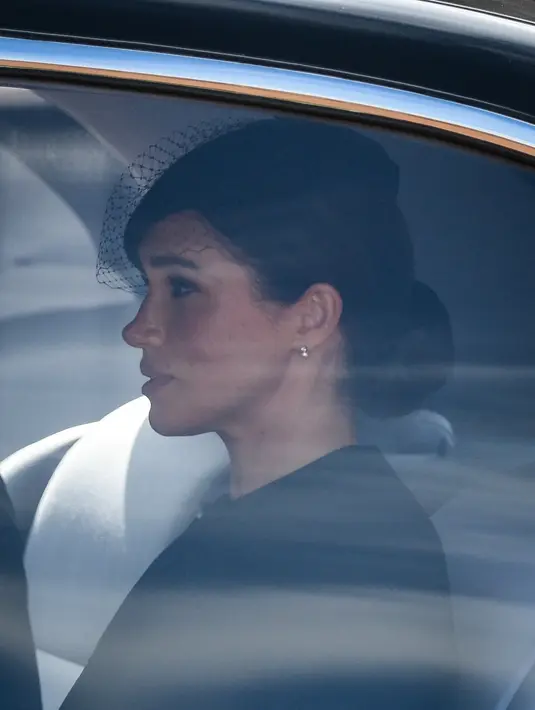 Meghan Markle berada di dalam mobil saat menghadiri prosesi persemayaman Ratu Elizabeth II di Westminster Hall di London (14/9/2022). Anting-anting ini dikenakan wanita 41 tahun tersebut saat ia melakukan tugas kerajaan pertama bersama Ratu Elizabeth II, tanpa Pangeran Harry. (Photo by Daniel LEAL/various sources/AFP)