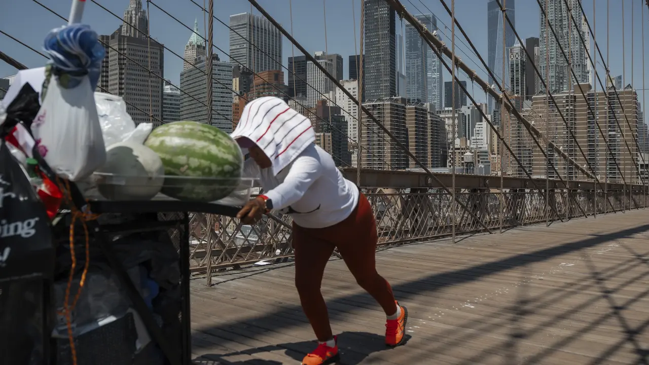 Seorang penjual buah mendorong gerobaknya di Jembatan Brooklyn saat gelombang panas di New York. (AP Photo/Olga Fedorova)