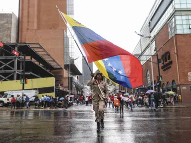 Seorang anggota milisi Venezuela memegang bendera nasional Venezuela selama pawai dukungan untuk mantan Presiden Venezuela Nicolas Maduro dalam sebuah unjuk rasa yang diselenggarakan oleh para pekerja di Caracas pada 14 Januari 2026. Pendukung pemerintah dan kelompok pro-Chavez turun ke jalan-jalan di Caracas, Venezuela, Rabu 14 Januari 2026. (Pedro MATTEY/AFP)
