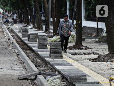 Pejalan kaki melintas saat pekerja menyelesaikan proyek revitalisasi pedestrian di kawasan Jalan Pattimura, Jakarta, Rabu (8/6/2022). Dinas Bina Marga DKI Jakarta merevitalisasi pedestrian dengan memperlebar menjadi tiga meter sehingga cukup luas untuk memberikan kenyamanan para pejalan kaki. (Liputan6.com/Faizal Fanani)