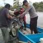 Personel Polsek Langgam jajaran Polres Pelalawan membantu mengangkat sepeda motor warga ke pompong untuk melintasi jalanan banjir. (Liputan6.com/M Syukur)