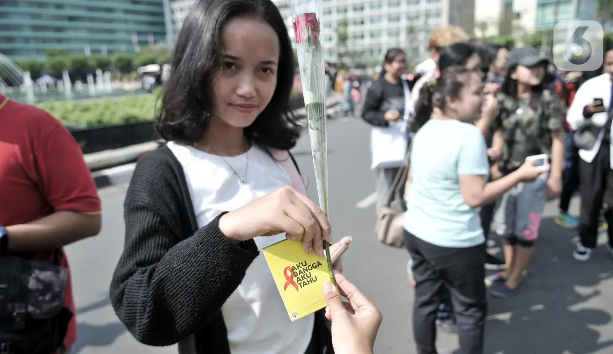 Seorang wanita menerima bunga mawar dan poster saat peringatan Hari AIDS Sedunia di Bundaran HI, Jakarta, Minggu (1/12/2019). Aksi yang digelar Pemuda Pancasila dan Depkes diisi dengan bagi bunga mawar beserta buku panduan tentang penyakit AIDS kepada warga. (merdeka.com/Iqbal S. Nugroho)