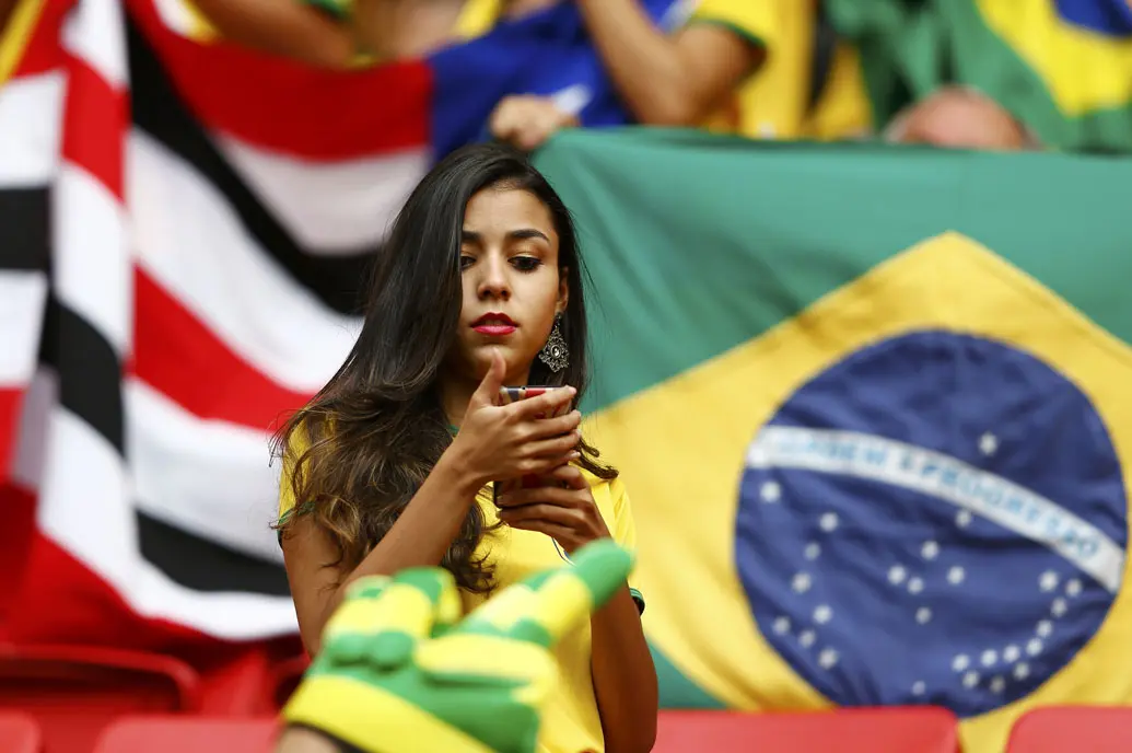 Sambil menunggu dimulainya laga Kamerun vs Brasil di Stadion Nasional Brasil, (23/6/2014), salah satu suporter Selecao terlihat memainkan ponselnya. (REUTERS/Dominic Ebenbichler)