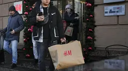Seorang pria membawa kantong belanja setelah meninggalkan toko utama H&M di Moskow, Rusia, Rabu (30/11/2022). Di hari terakhir pembukaan, H&M menjual seluruh persediaan dengan diskon besar-besaran. (AP Photo/Alexander Zemlianichenko)