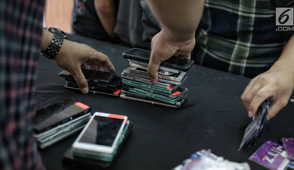 Polisi merapikan barang bukti kasus order fiktif pada transportasi online saat rilis di Polda Metro Jaya, Jakarta, Rabu (13/2). Kasus ini berhasil diungkap oleh Satgas Cyber Crime Polda Metro Jaya. (Liputan6.com/Faizal Fanani)