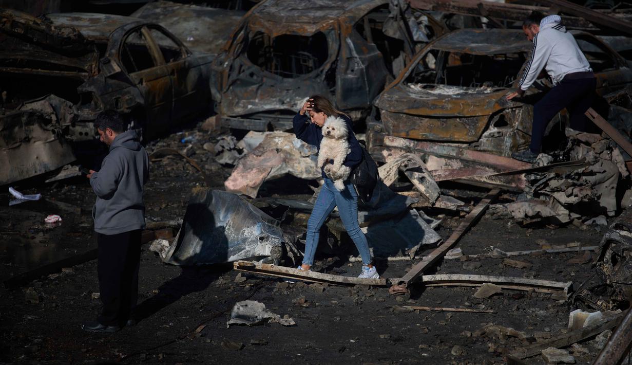 Seorang wanita menggendong anjingnya saat berjalan melewati mobil-mobil yang terbakar sehari setelah serangan udara Israel di Beirut, Lebanon, Kamis 9 April 2026. Israel terus melancarkan serangan besar-besaran terhadap Lebanon. (AP Photo/Emilio Morenatti)