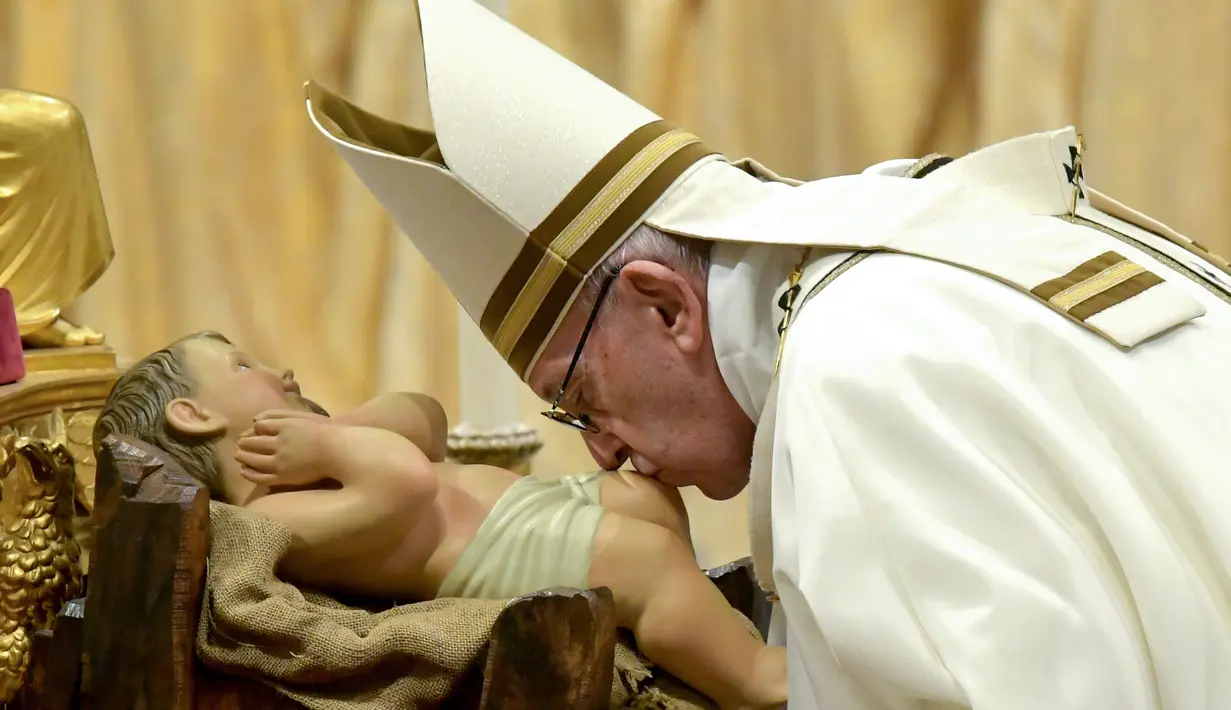 Paus Fransiskus mencium patung bayi Yesus saat misa Natal di Basilika Santo Petrus, Vatikan, (24/12). Paus menyerukan kepada masyarakat di negara maju agar menjalani kehidupan yang sederhana dan tidak terlalu materialistis. (AFP Photo/Tiziana Fabi)