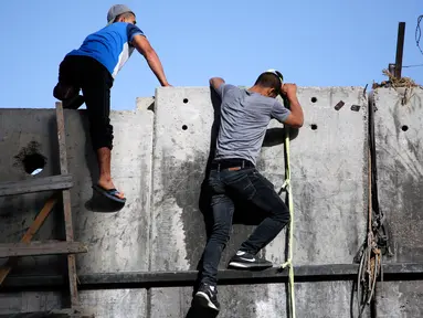 Dua pemuda Palestina menggunakan tangga berusaha memanjat tembok pembatas Israel saat berangkat untuk beribadah salat Jumat di Masjid Al-Aqsa, Yerusalem, Jumat (9/6). (AFP Photo/Abbas Momani)