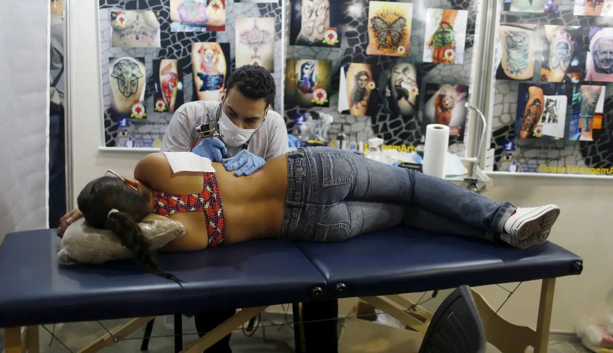 Seorang seniman terlihat serius menato seorang perempuan dibagian samping dadanya saat Festival Internasional Tattoo Week Rio 2016 ketiga di Rio de Janeiro, Brasil, (22/1/2016). (REUTERS/Pilar Olivares)