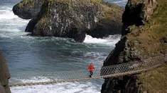 Seorang wisatawan berdiri di tengah Jembatan Carrick-a-Rede Rope di Pantai Causeway, Irlandia Utara, Rabu (8/4/2015). Jembatan tersebut diperkirakan telah dibangun selama lebih dari 350 tahun oleh para nelayan salmon. (REUTERS/Cathal McNaughton)