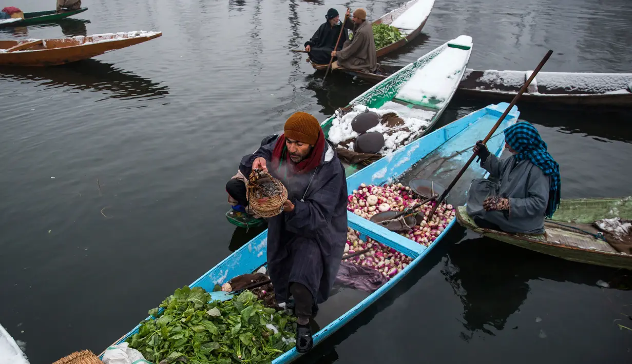 Pedagang mempersiapkan Kangri atau pot api tradisional untuk menghangatkan tubuhnya saat berdagang ditengah dinginnya salju di pasar terapung di danau Dal, Srinagar, Kashmir India, (25/1). (AP Photo/Dar Yasin)