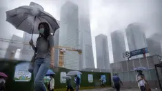 Para komuter yang mengenakan masker dan membawa payung berjalan melintasi alun-alun saat hujan pagi di kawasan pusat bisnis di Beijing, China, 12 Juli 2022. Beijing telah membatalkan rencana untuk mengizinkan hanya orang yang divaksinasi yang memasuki ruang publik. (AP Photo/Mark Schiefelbein)